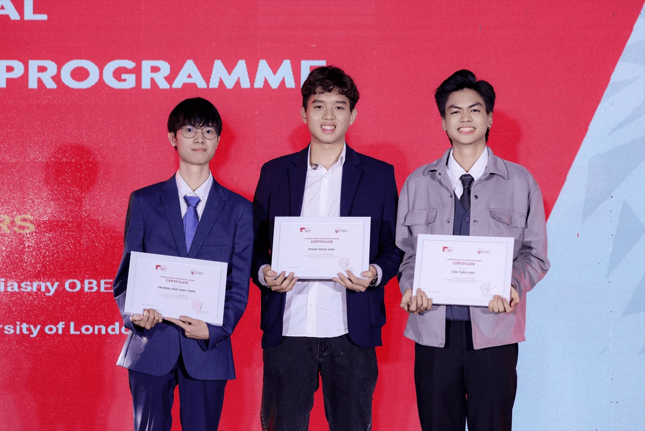 Three BUV students pose on stage holding award certificates during a programme ceremony.