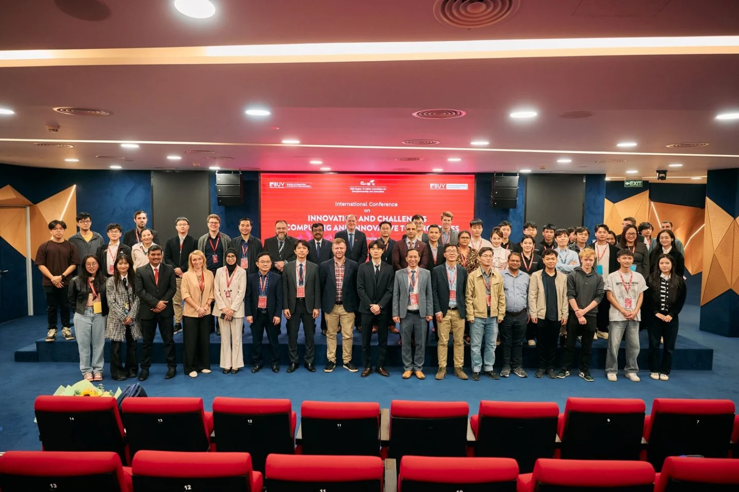 A large group of students, faculty, and guests pose on stage at a BUV event in an auditorium.