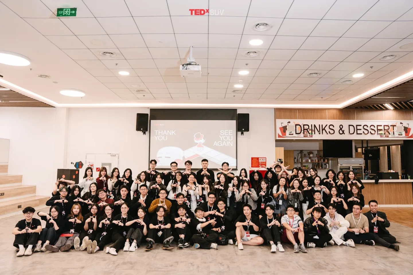 A large group of BUV students pose together in a campus hall beneath a TEDx sign, with a “Drinks & Desserts” counter in the background.