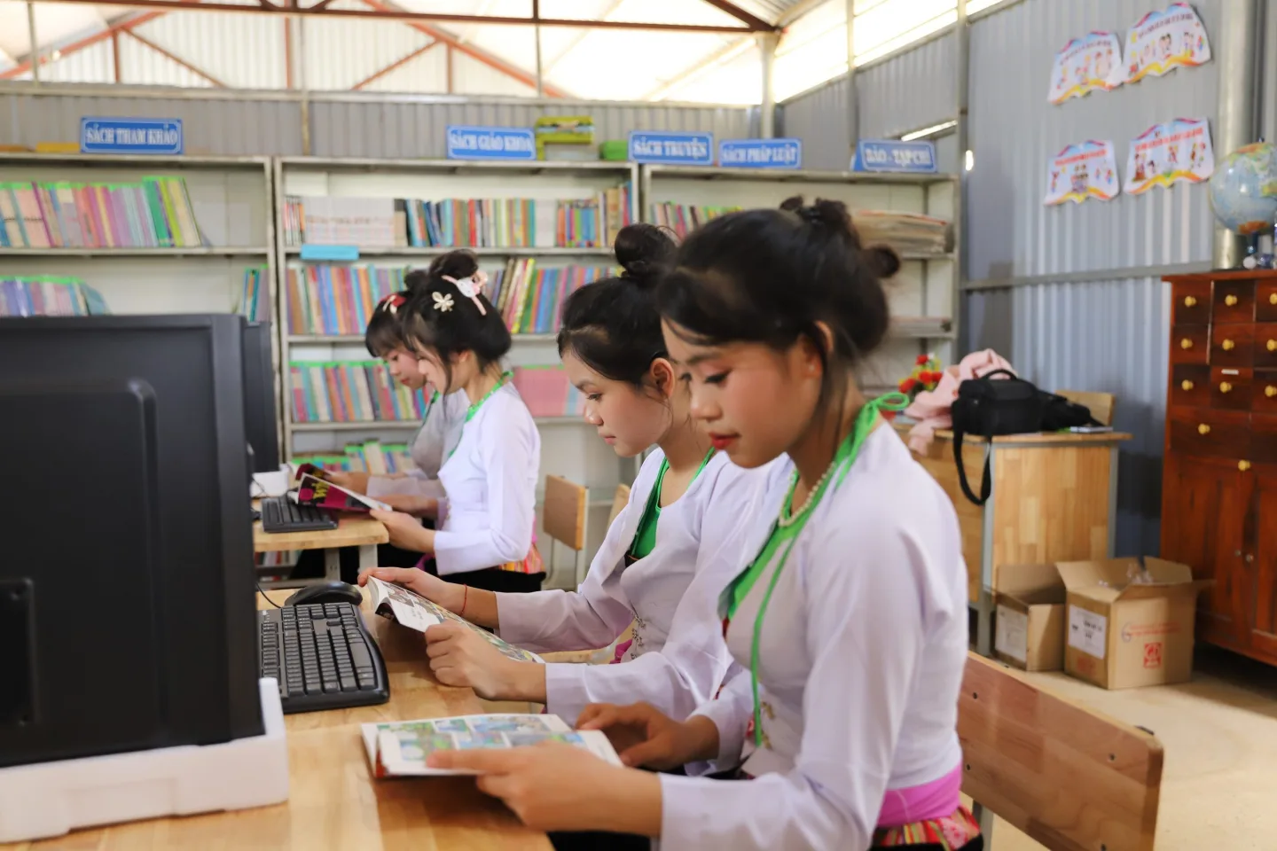Students in white uniforms study books and use computers in a school library.