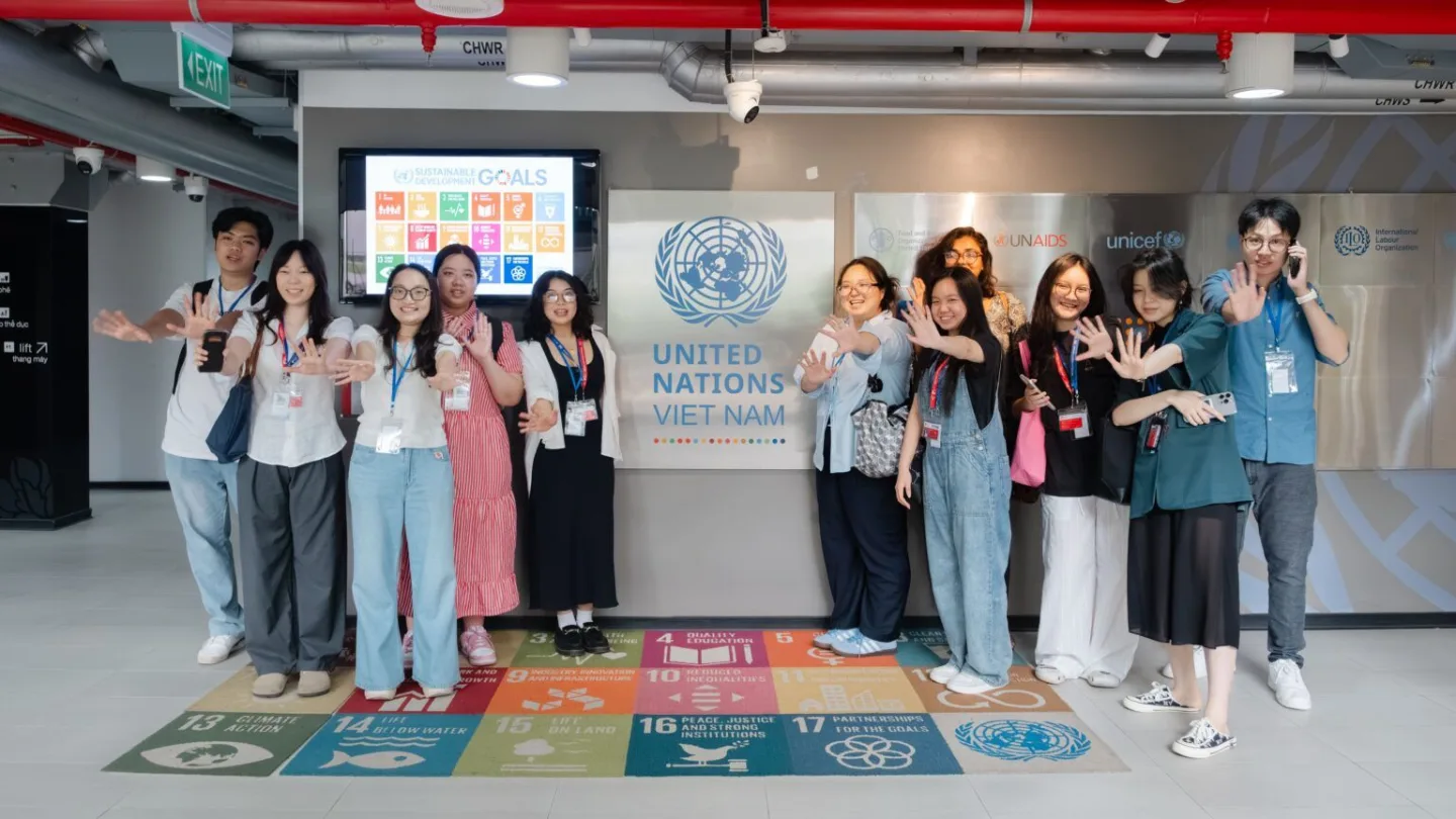 A group of students posing in front of a United Nations Vietnam display, with colorful Sustainable Development Goals panels on the floor.