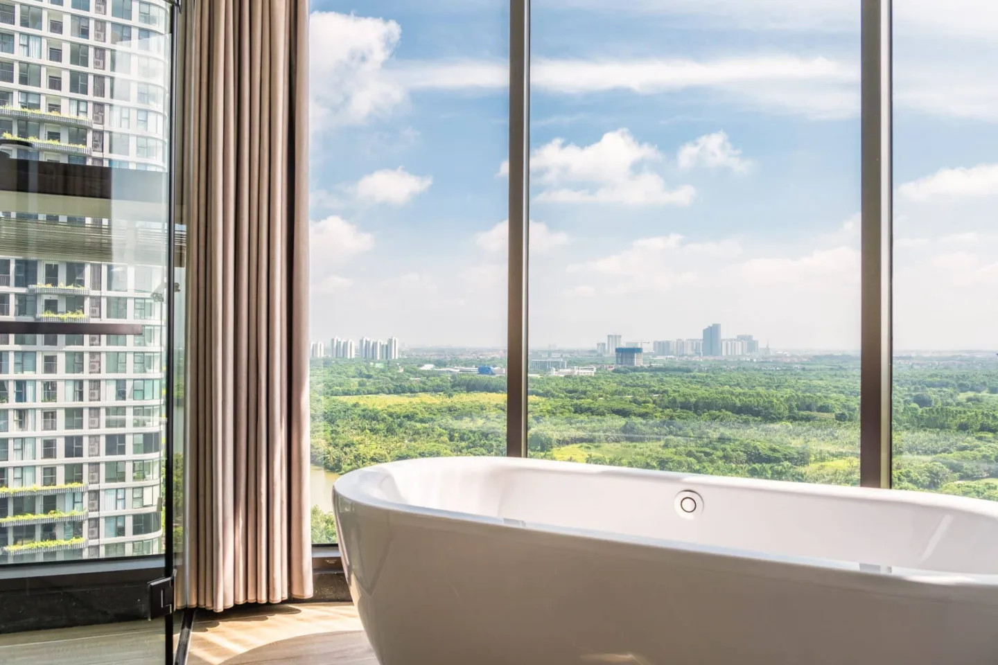 Freestanding bathtub beside floor-to-ceiling windows overlooking Ecopark’s lush greenery and distant skyline.