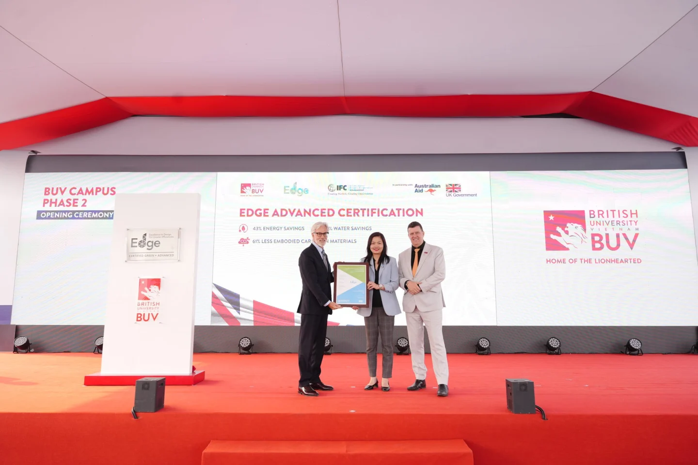 Three representatives pose with a certificate onstage during the EDGE Advanced Certification ceremony at BUV Campus Phase 2.