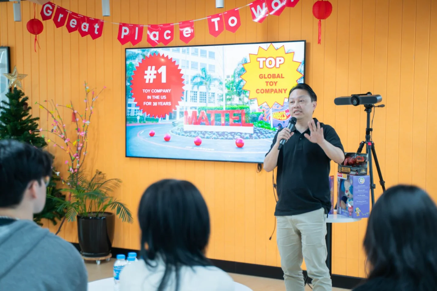 A speaker addresses an audience at BUV beneath a “Great Place to Work” banner, with a screen highlighting the university’s workplace achievements.