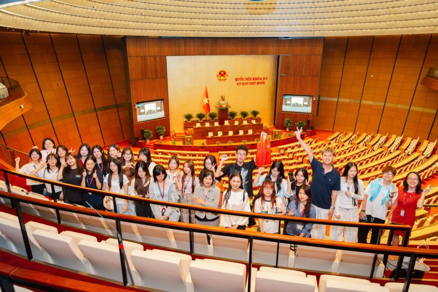 A group of students posing in the gallery of a Vietnamese government assembly hall.