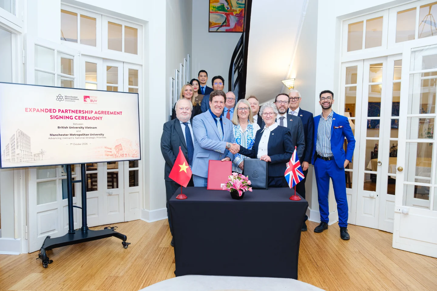 BUV and Manchester Metropolitan University representatives at the expanded partnership agreement signing ceremony, with Vietnamese and UK flags.
