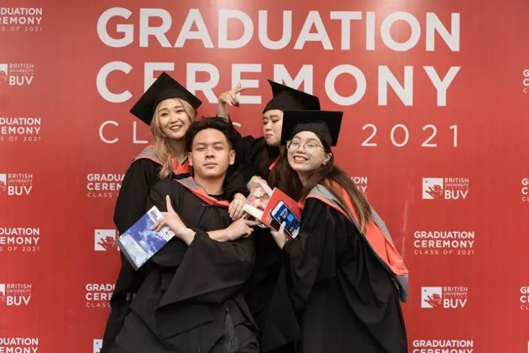 Graduation Ceremony 2021 at British University Vietnam (BUV): a group of graduates in black gowns and mortarboards pose and smile for the camera in front of the “Graduation Ceremony 2021” backdrop.