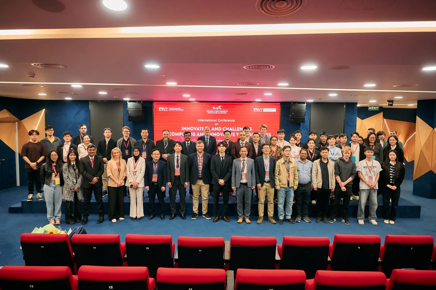 A large group of students, faculty, and guests pose on stage at a BUV event in an auditorium.