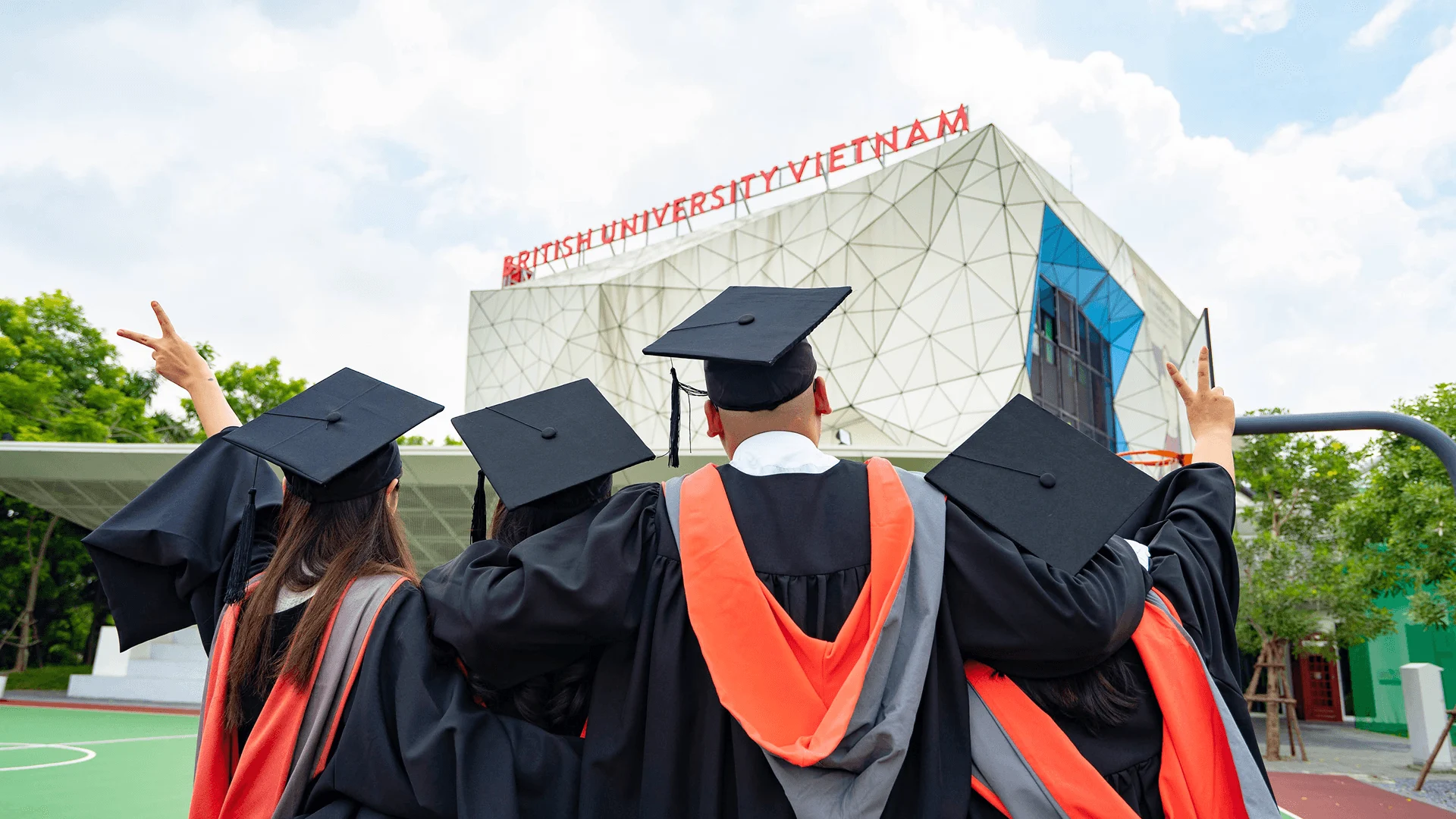 BUV postgraduate graduates in caps and gowns celebrating outside the British University Vietnam campus