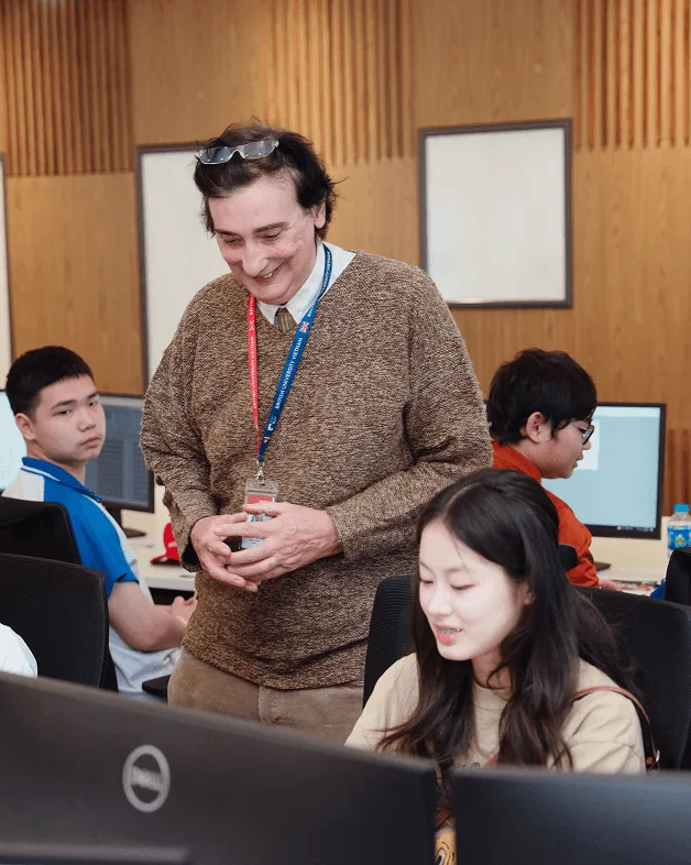 An instructor stands among students working at computers in a university classroom.