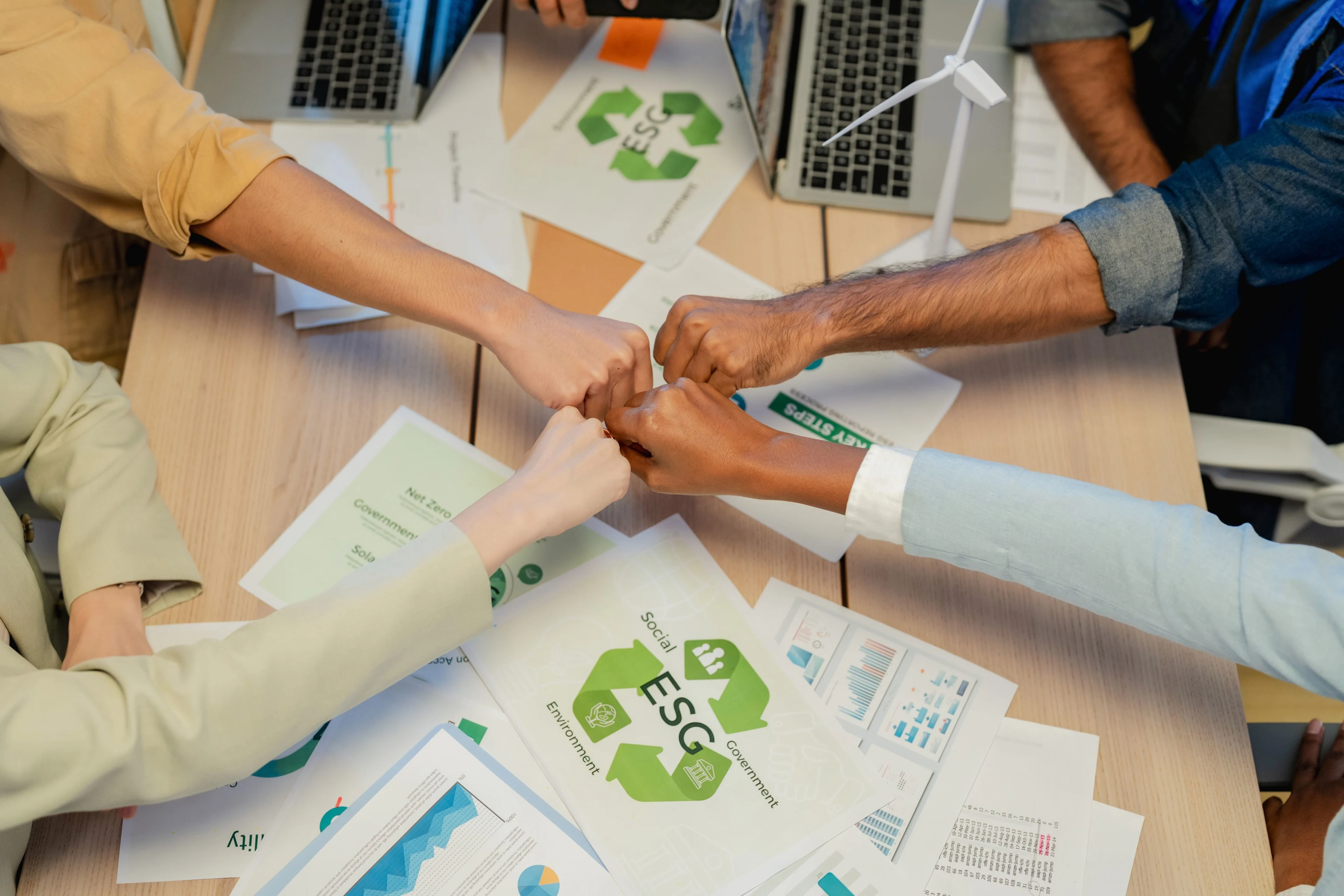 BUV students fist-bump during an ESG sustainability project with reports, laptops and a wind turbine model.