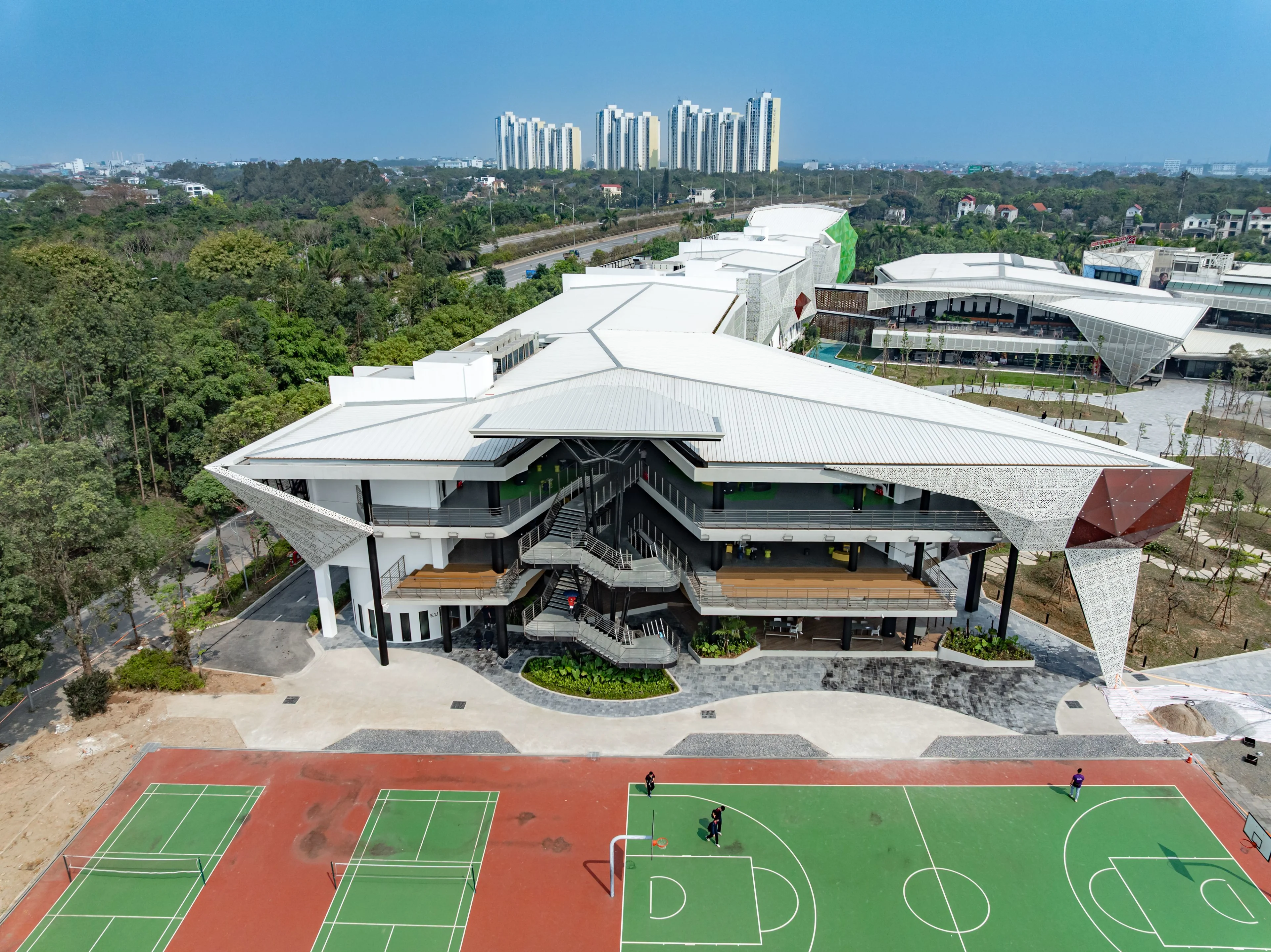 Aerial view of BUV’s modern campus, featuring a white-roofed academic building, outdoor basketball and tennis courts, surrounding greenery, and high-rise buildings in the distance.