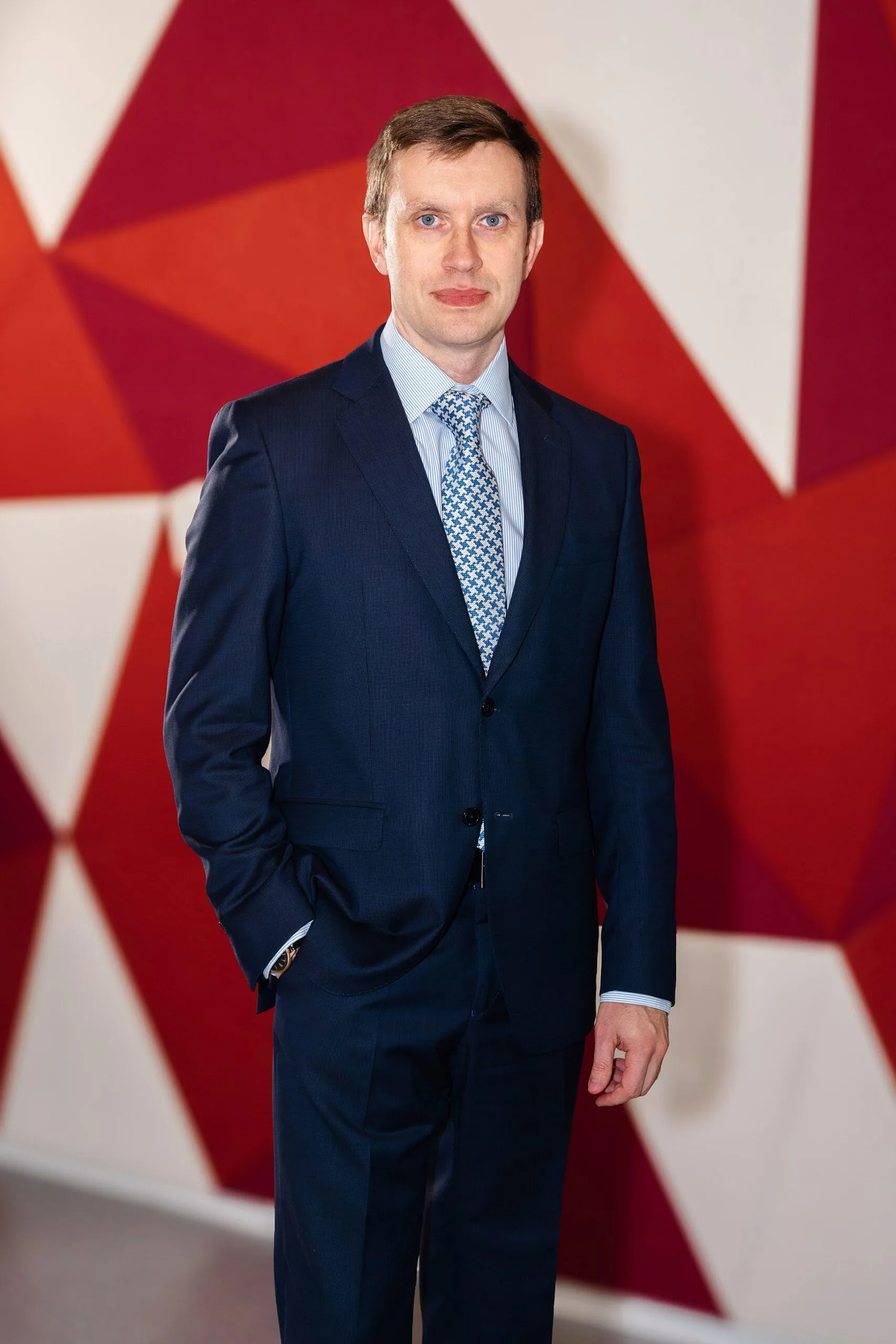 Portrait of Vladimir Antchak in a dark suit and patterned tie, standing in front of a red-and-white flag backdrop.