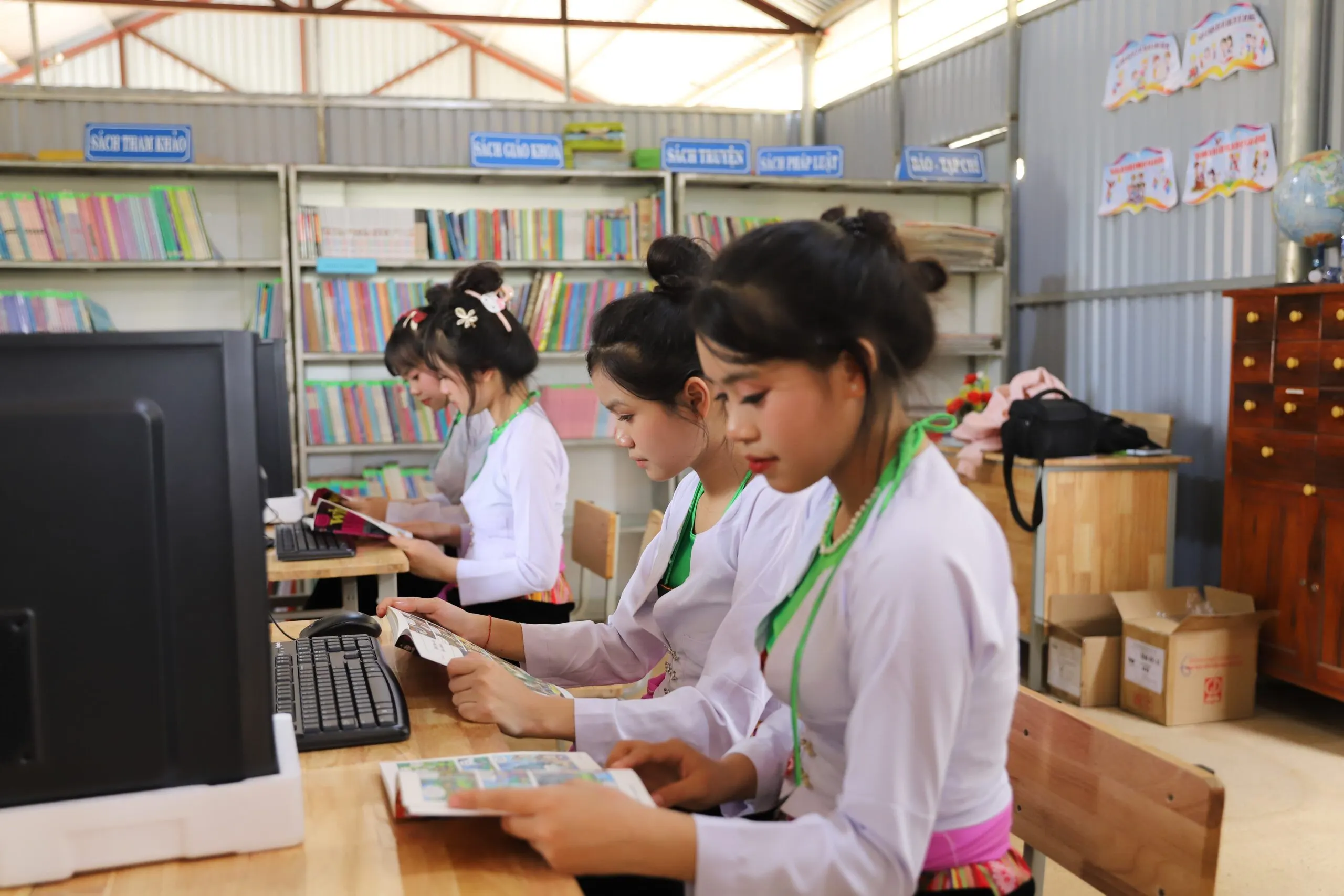 Students in white uniforms study books and use computers in a school library.