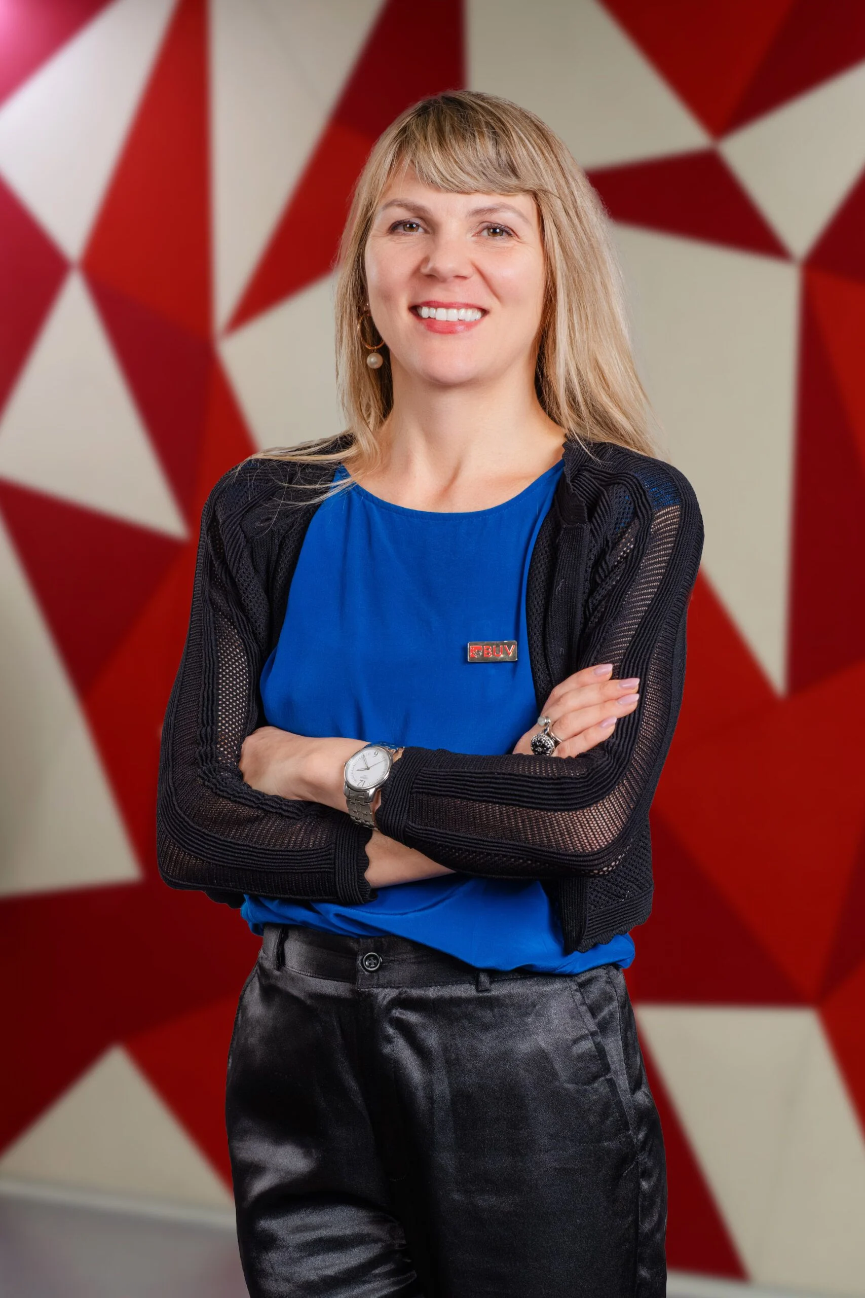 Ramona Anna, BUV staff member, smiling with folded arms against a red geometric background