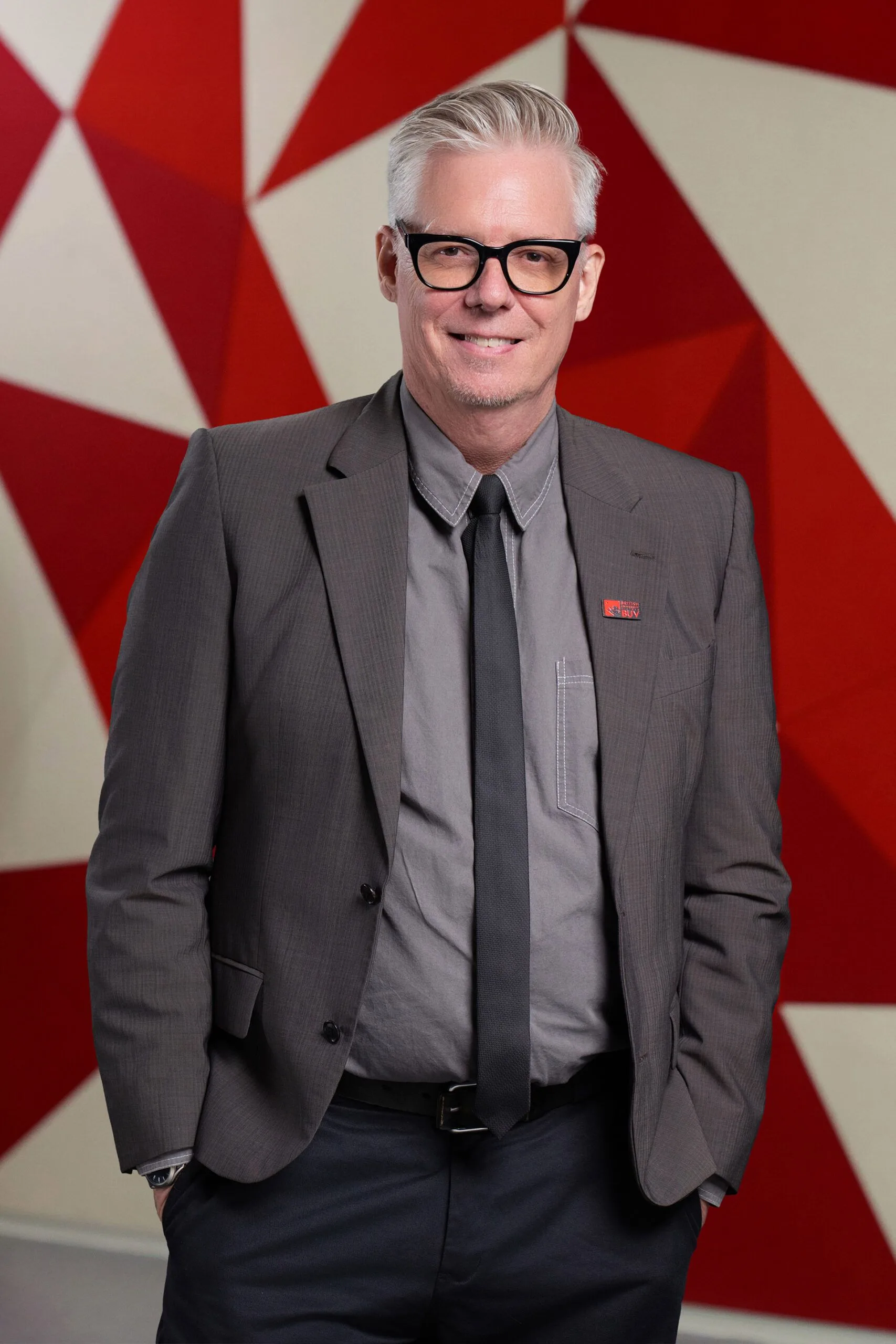 Don Hickerson in formal attire at British University Vietnam against a red geometric backdrop
