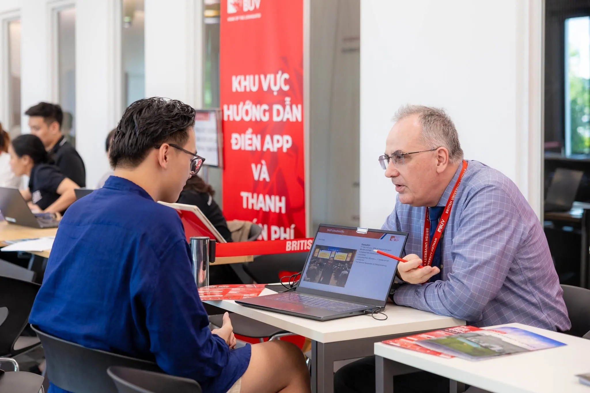 A British University Vietnam staff member advises a prospective student at an admissions and tuition guidance desk.