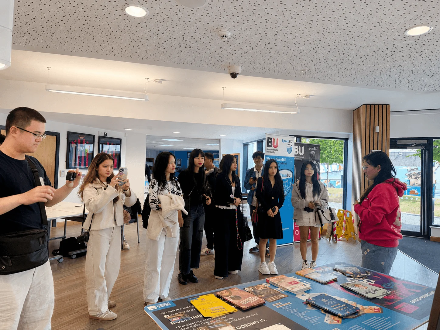 A group of students listening to a guide near an information table during a campus visit to Bournemouth University.