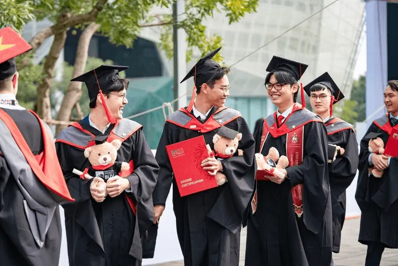 BUV graduates in caps and gowns celebrating together while holding diplomas and teddy bears.