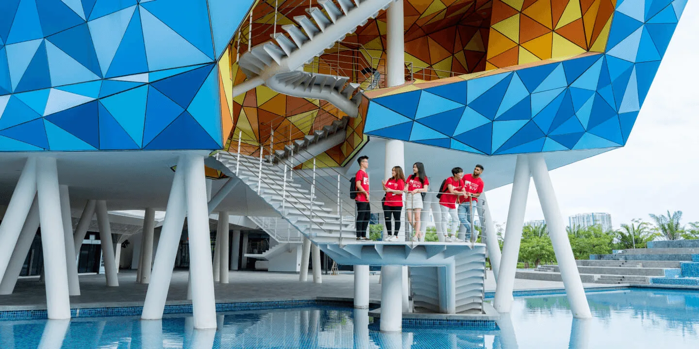 Sinh viên BUV đứng trên cầu thang bên ngoài khuôn viên hiện đại với kiến trúc đa giác xanh nổi bật.