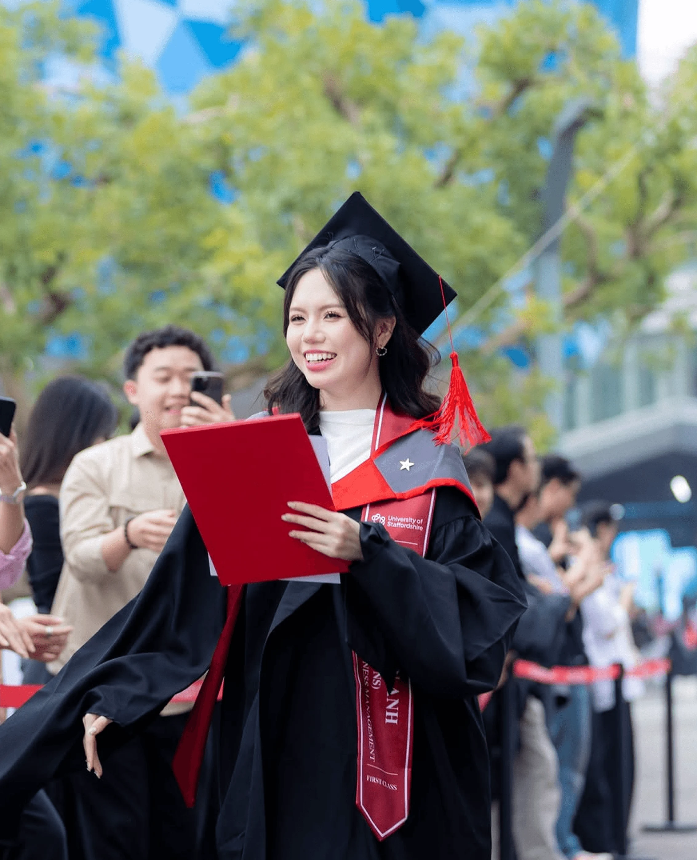 A smiling female graduate in a graduation gown holding her degree certificate.