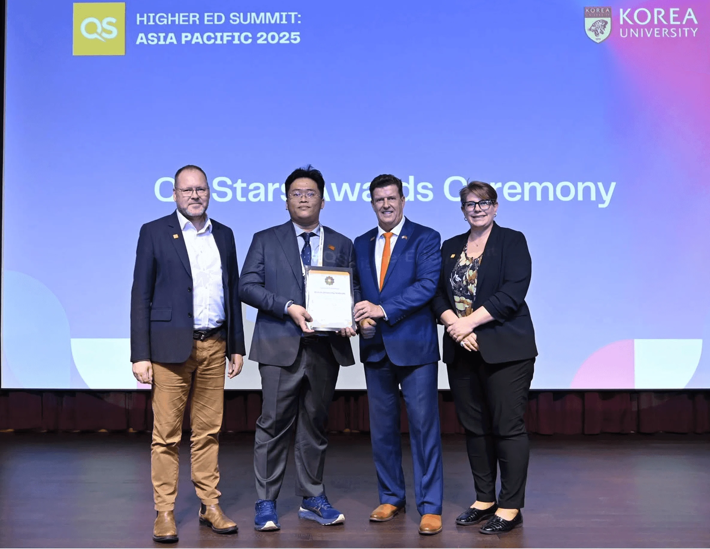Four representatives pose on stage as a British University Vietnam delegate receives a certificate at the QS Higher Ed Summit: Asia Pacific 2025 awards ceremony.
