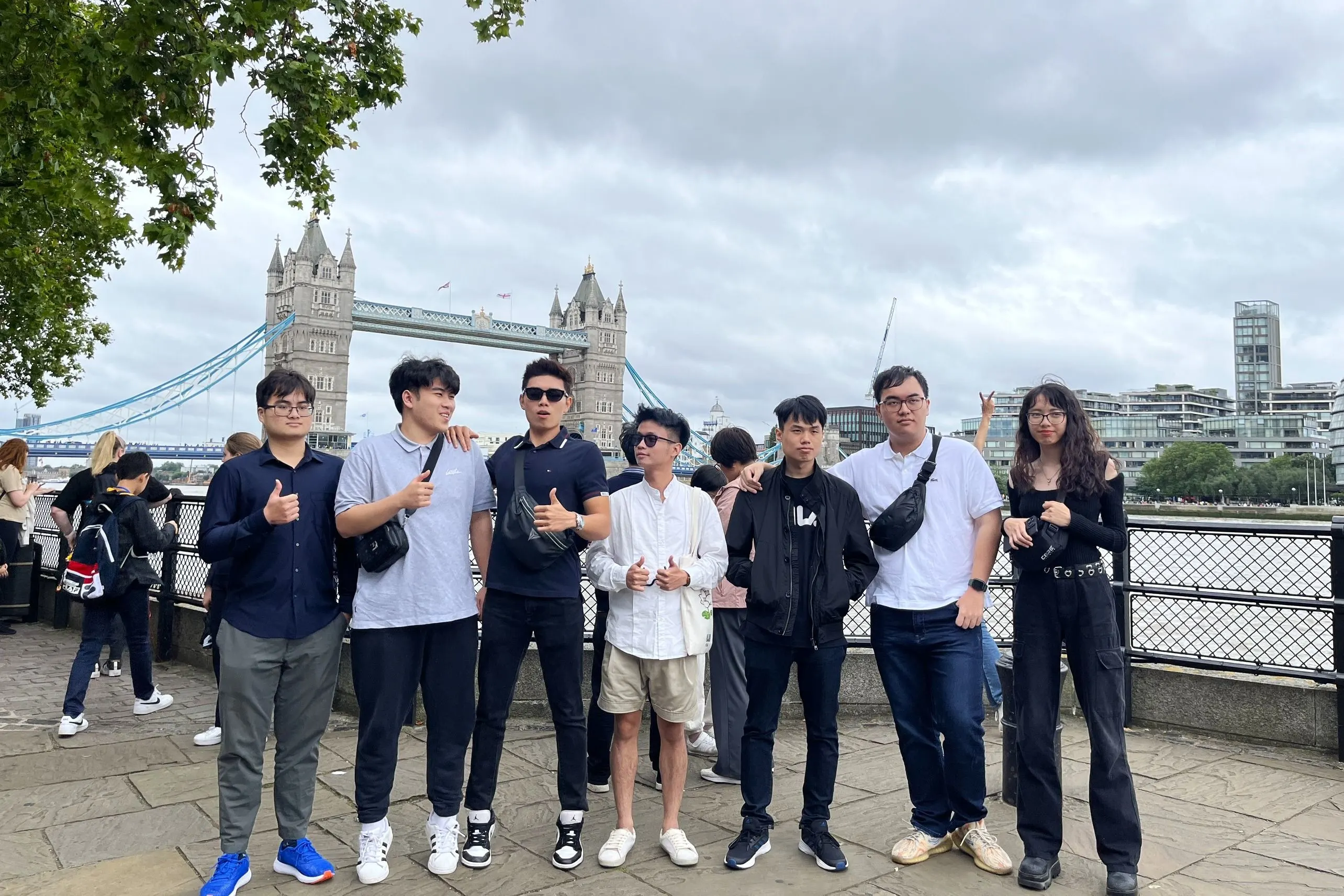 Group of students posing by the River Thames with Tower Bridge in the background during a London tour.
