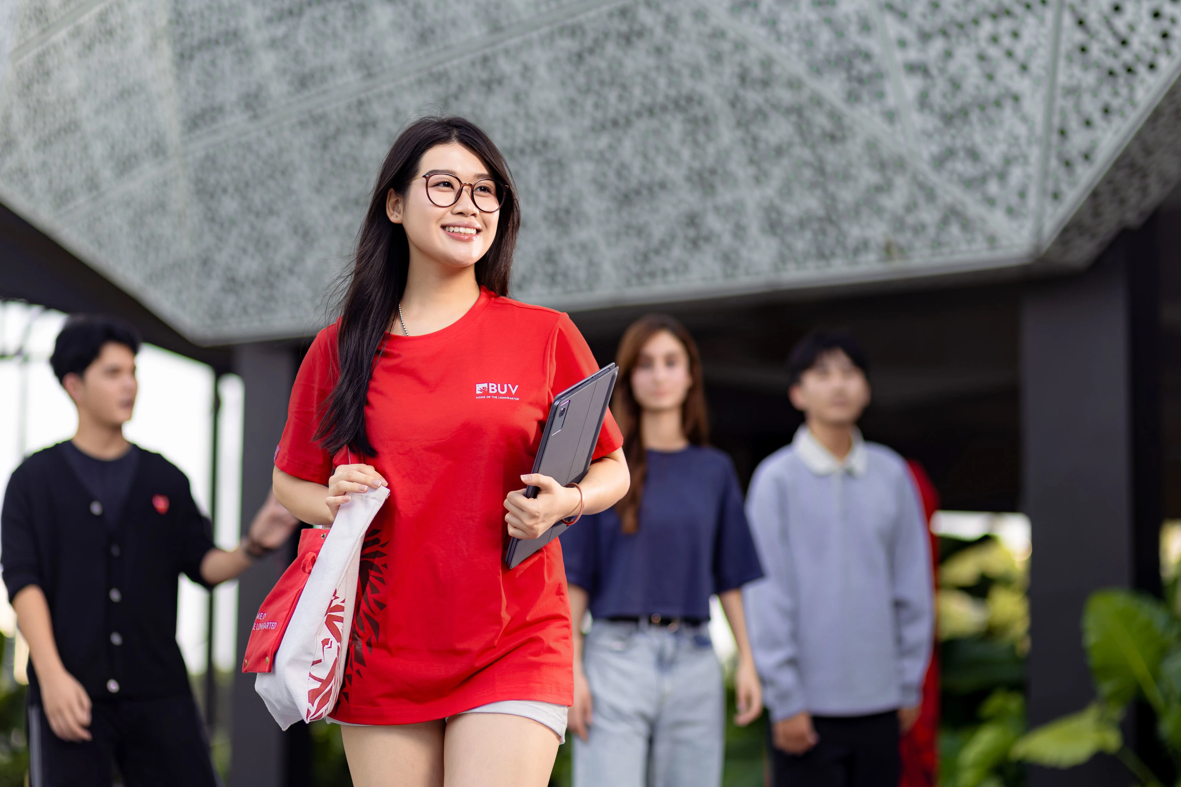 Sinh viên British University Vietnam mặc áo đỏ BUV, cầm máy tính bảng cùng bạn bè trong khuôn viên trường