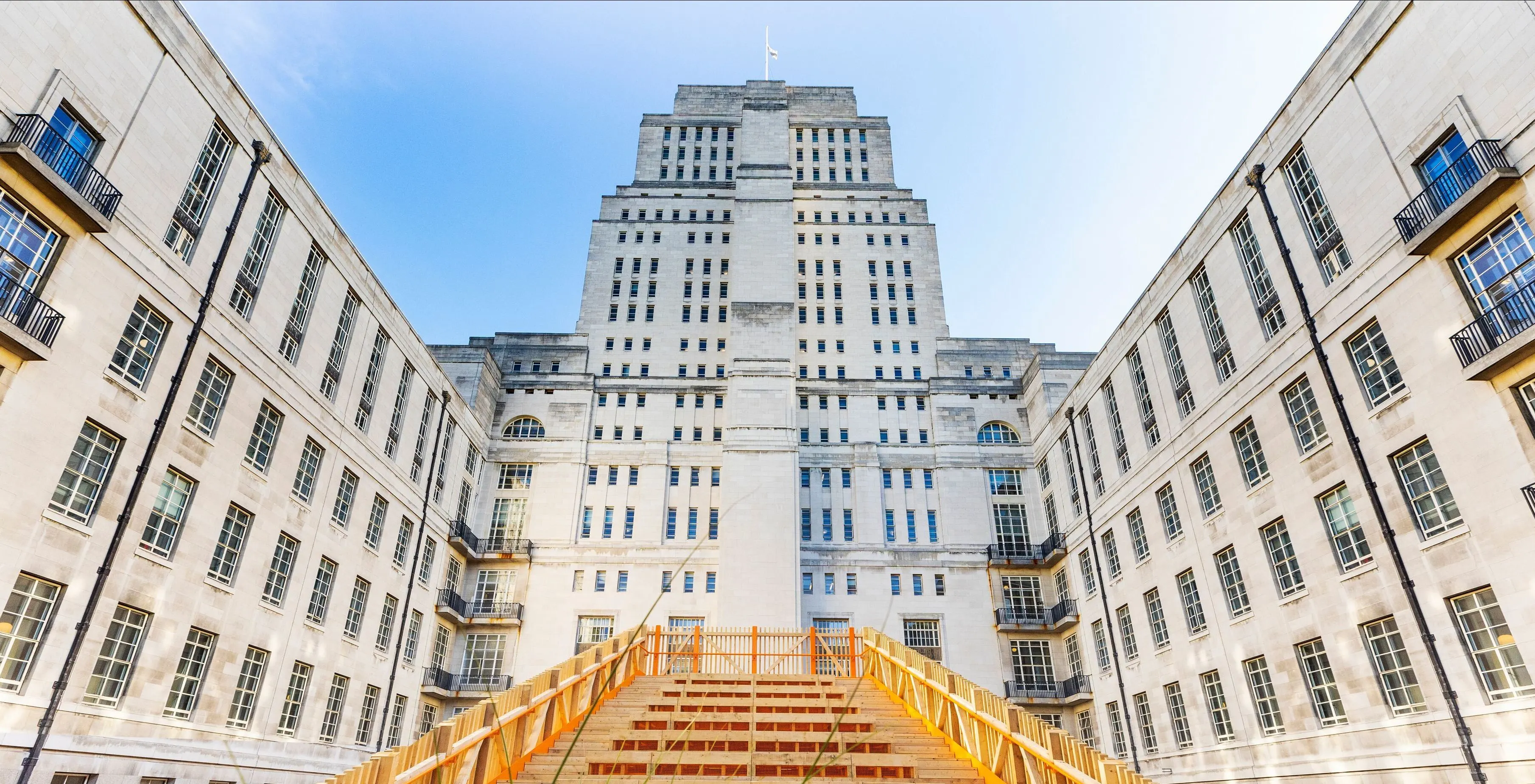 People gather around a large orange staircase installation in the courtyard of a University of London building.