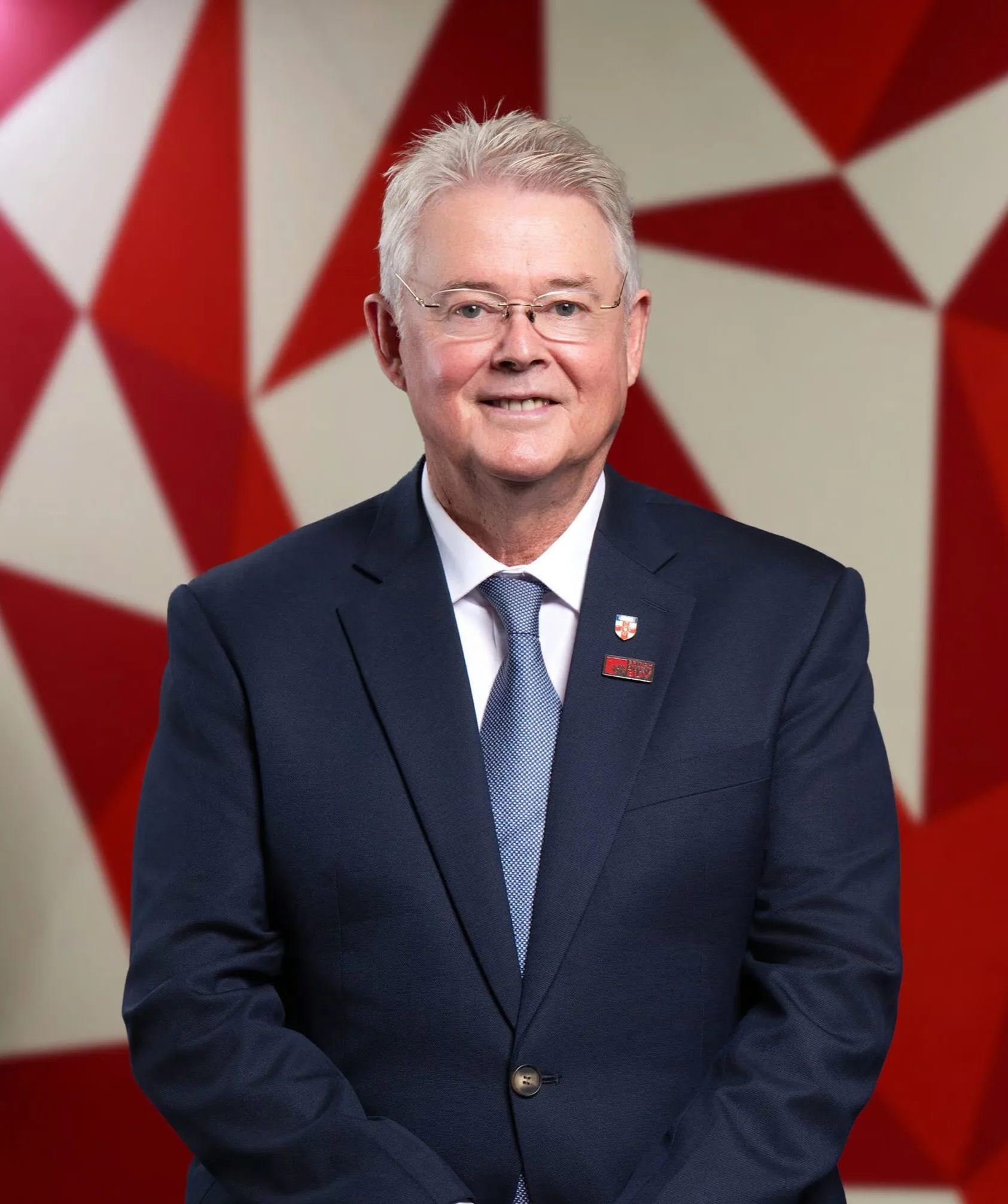 Portrait of R. D. Gordon smiling in a navy suit and tie against a red-and-white geometric background.