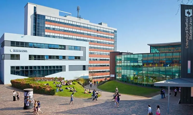 Staffordshire University campus with modern academic buildings, glass façades, landscaped lawns, and students walking through the courtyard.