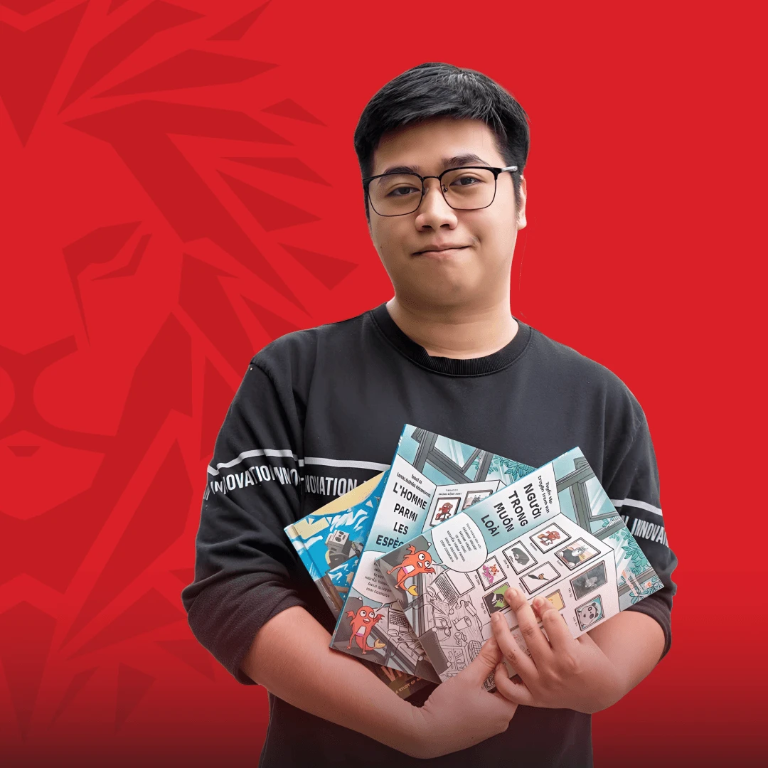BUV alumnus wearing glasses and holding several illustrated books against a red background.