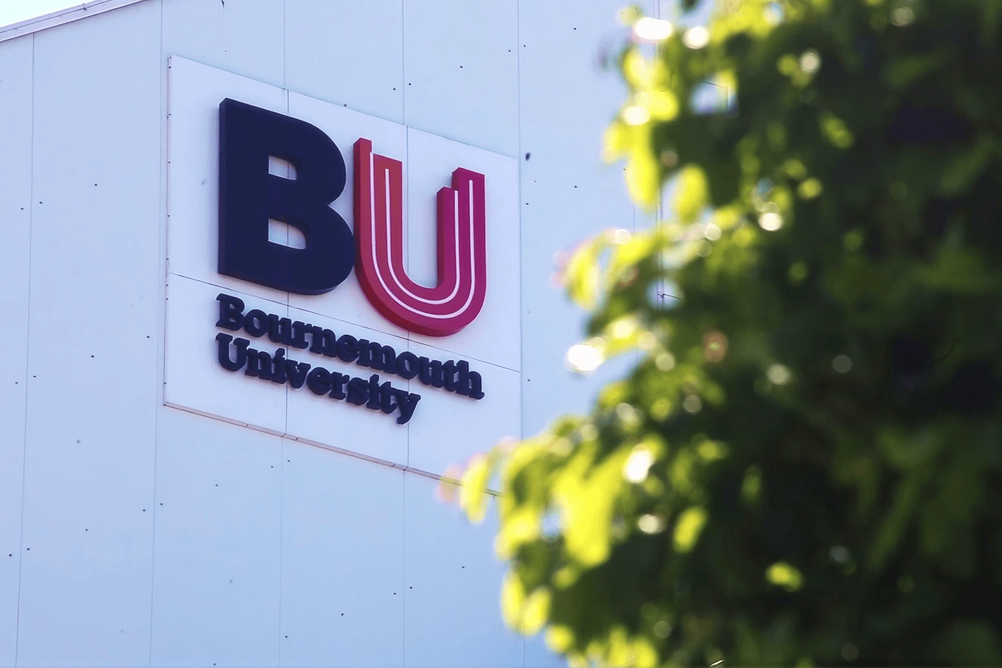 Bournemouth University campus building with BU logo and university sign framed by greenery