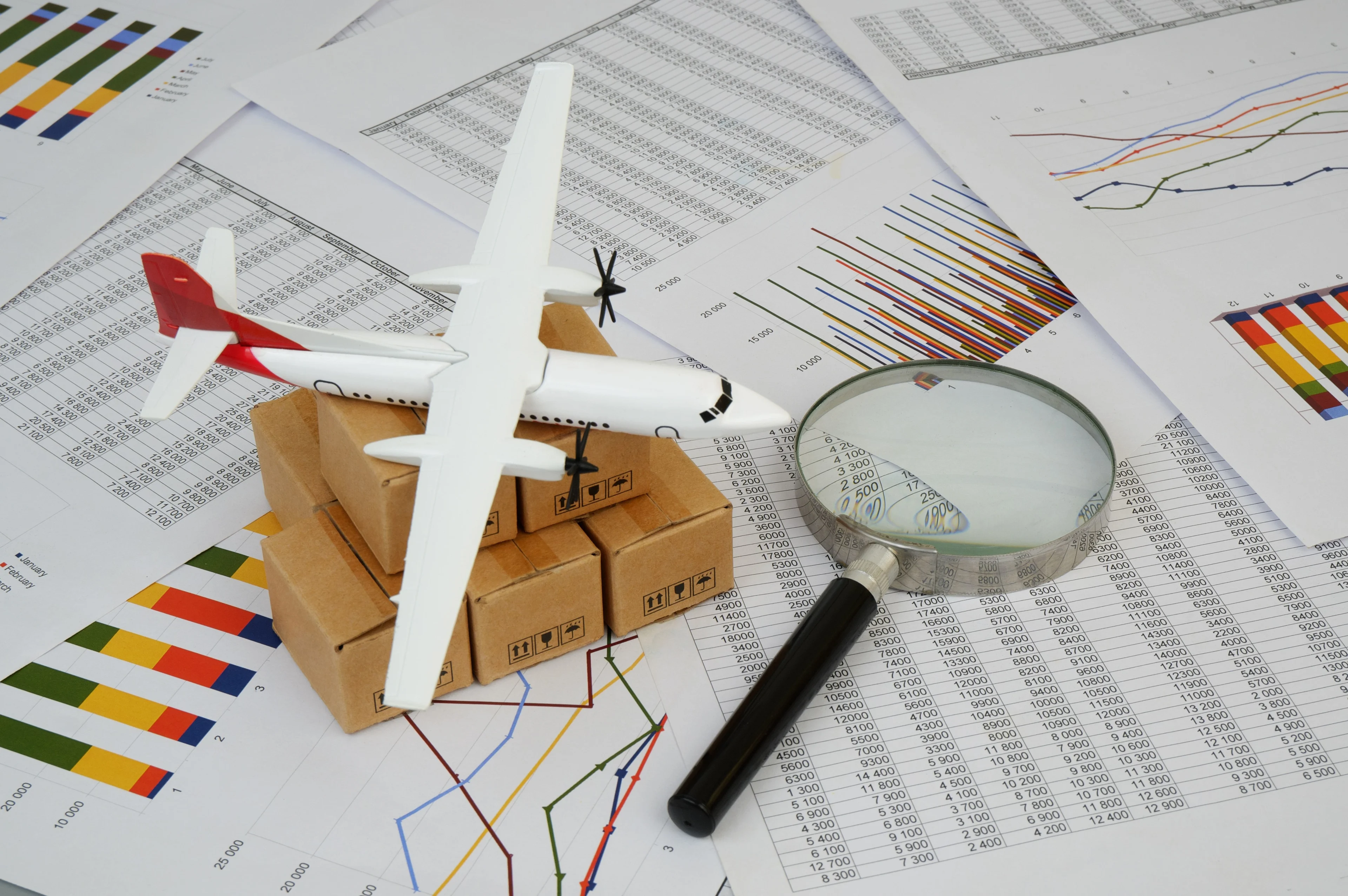 Model airplane, parcels and magnifying glass on logistics data charts for supply chain analysis