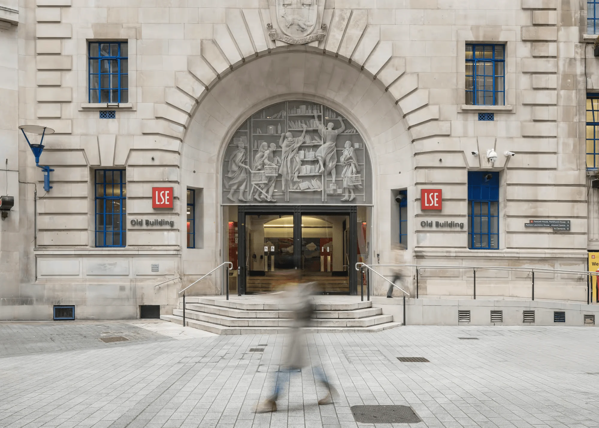 Main entrance of the London School of Economics and Political Science, with a blurred pedestrian walking past.