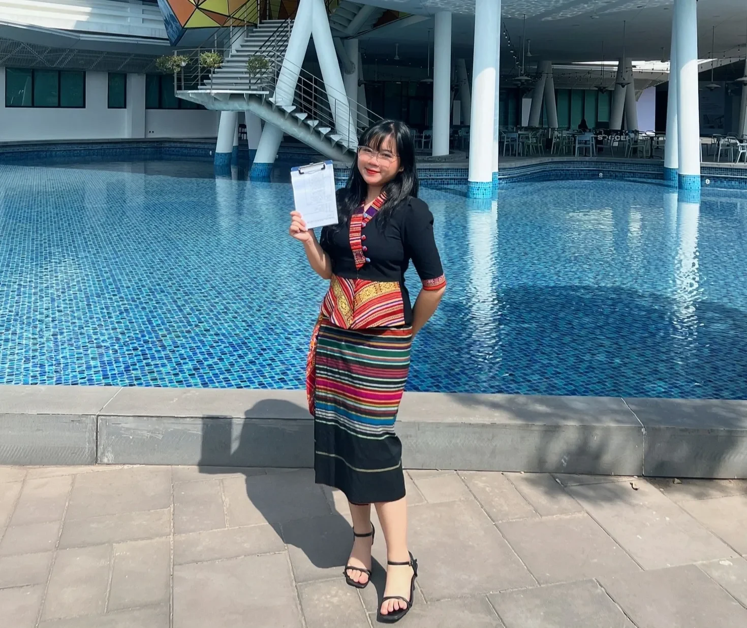 BUV student Thi Quynh Anh holds a Lion Heart Scholarship certificate beside the campus pool.