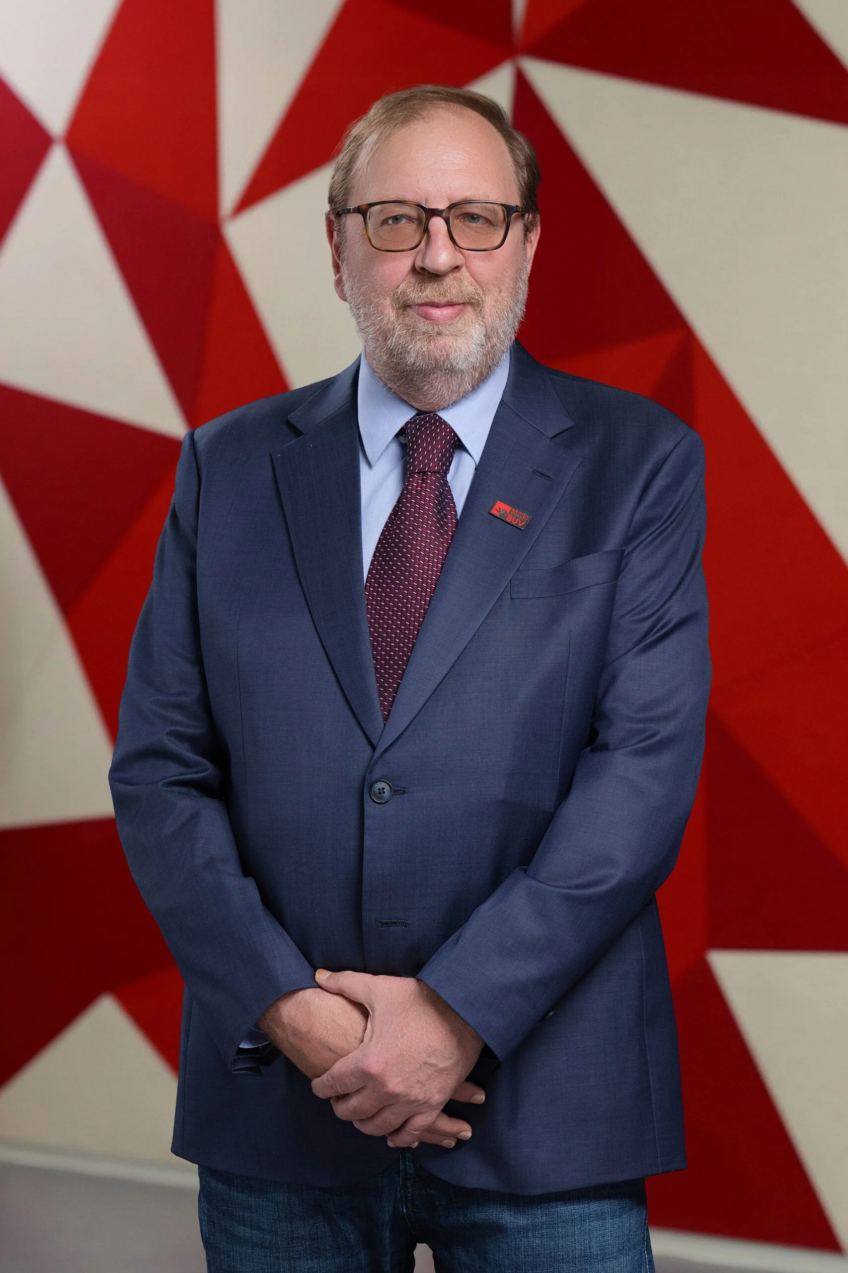 Dr Giovanni Merola in a navy suit wearing a British University Vietnam pin against a red geometric backdrop