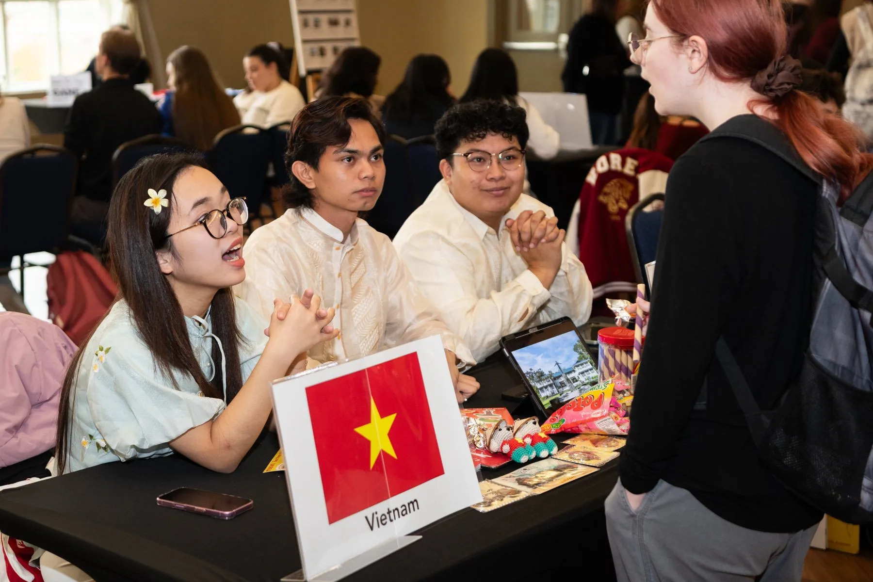 Students representing Vietnam confidently speak with an attendee at a cultural exchange event booth.