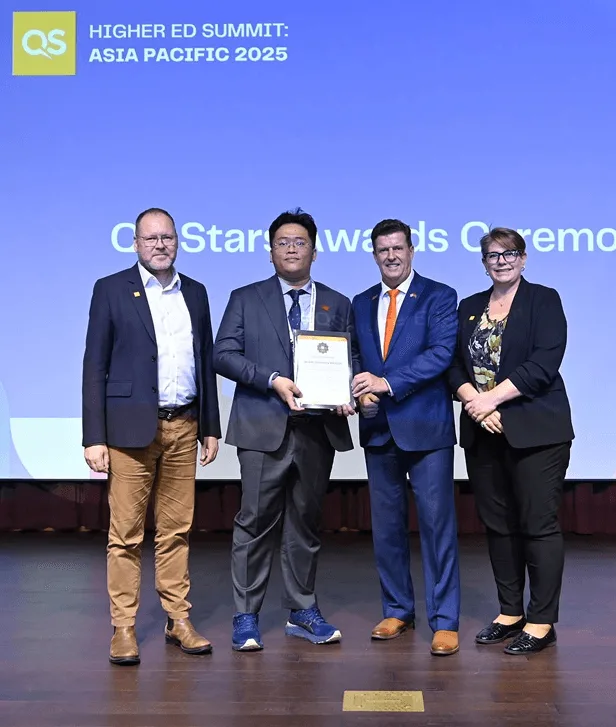 Four representatives pose on stage as a British University Vietnam delegate receives a certificate at the QS Higher Ed Summit: Asia Pacific 2025 awards ceremony.