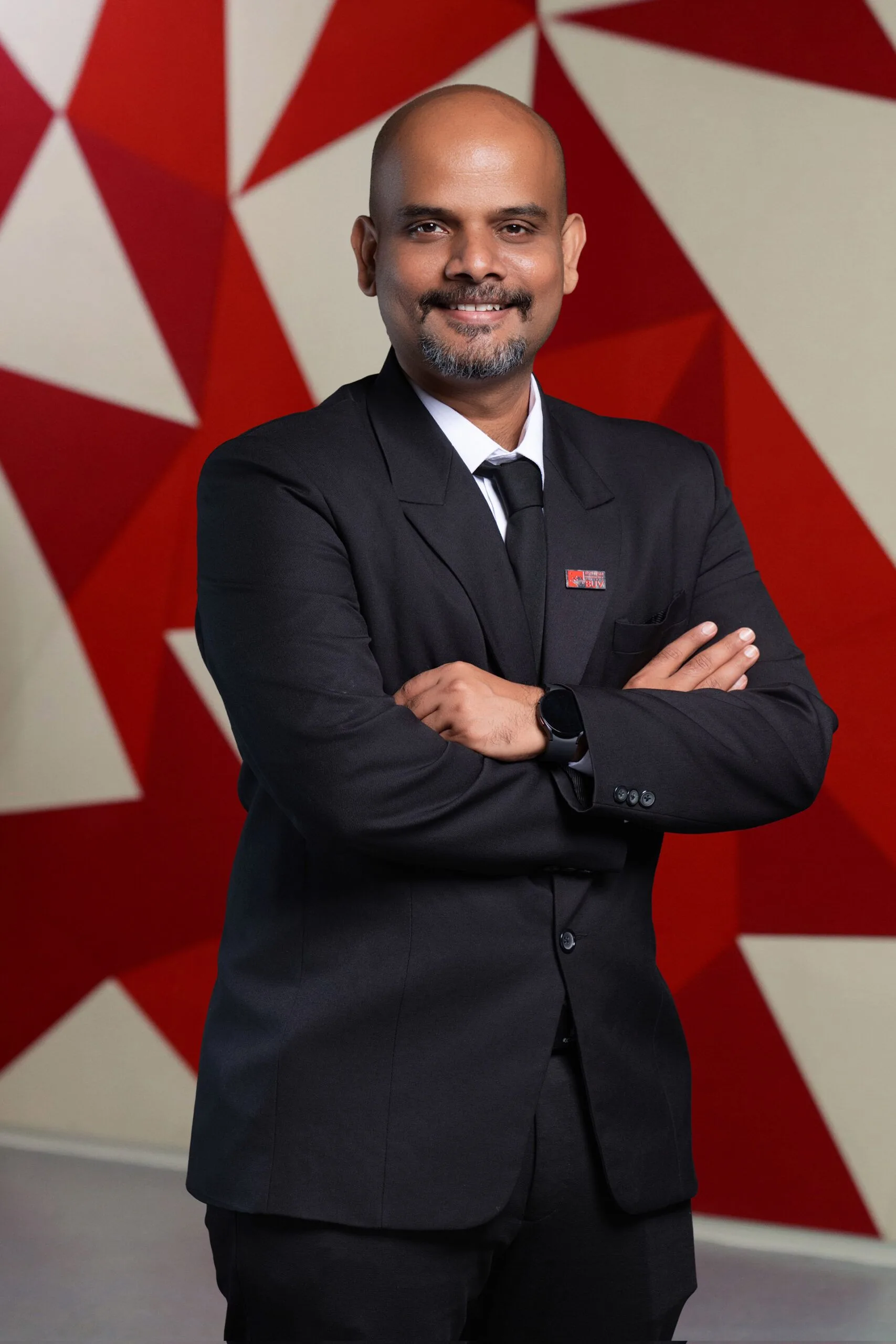 Dr Sriganeshvarun in a black suit at British University Vietnam against a red geometric backdrop