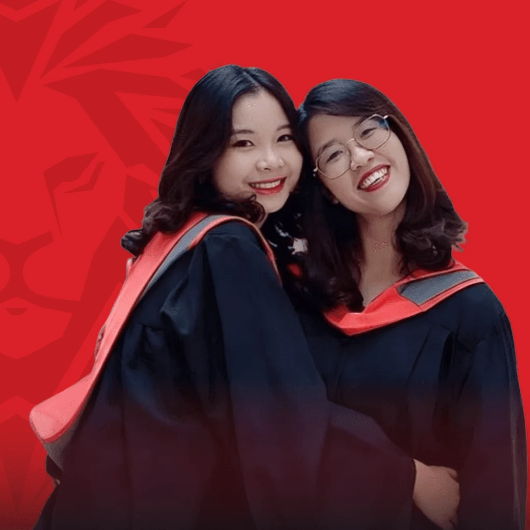 Two smiling BUV alumnae in black graduation gowns with red-trimmed hoods pose together against a red background.