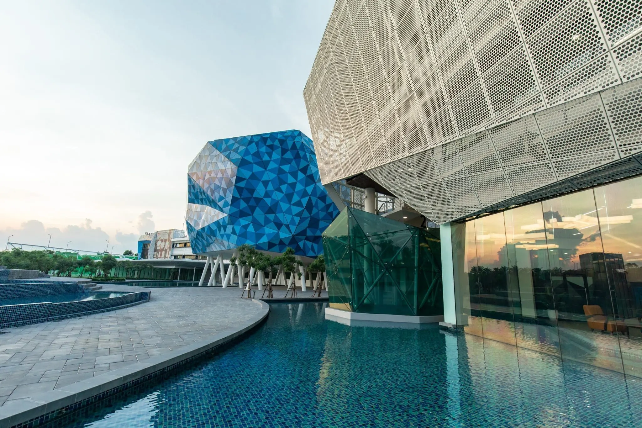 Modern BUV campus buildings with geometric blue and silver façades reflected in a landscaped pool at sunset.