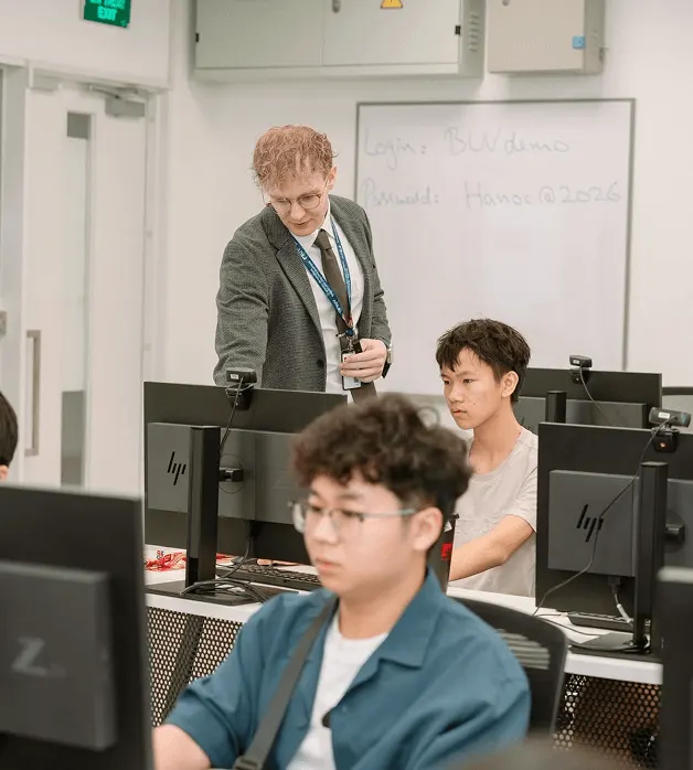A lecturer assists students working at desktop computers in a university computer lab.