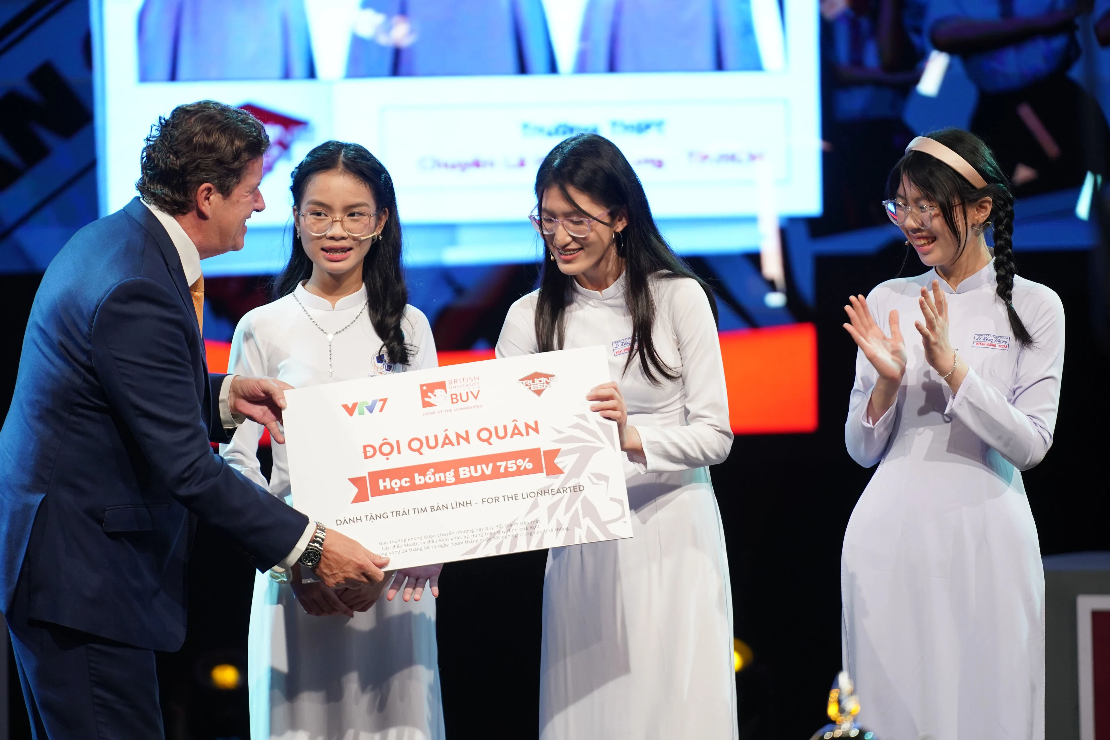 BUV awards a 75% scholarship to students in white áo dài on stage, presenting a sign reading “Đội Quán Quân.”