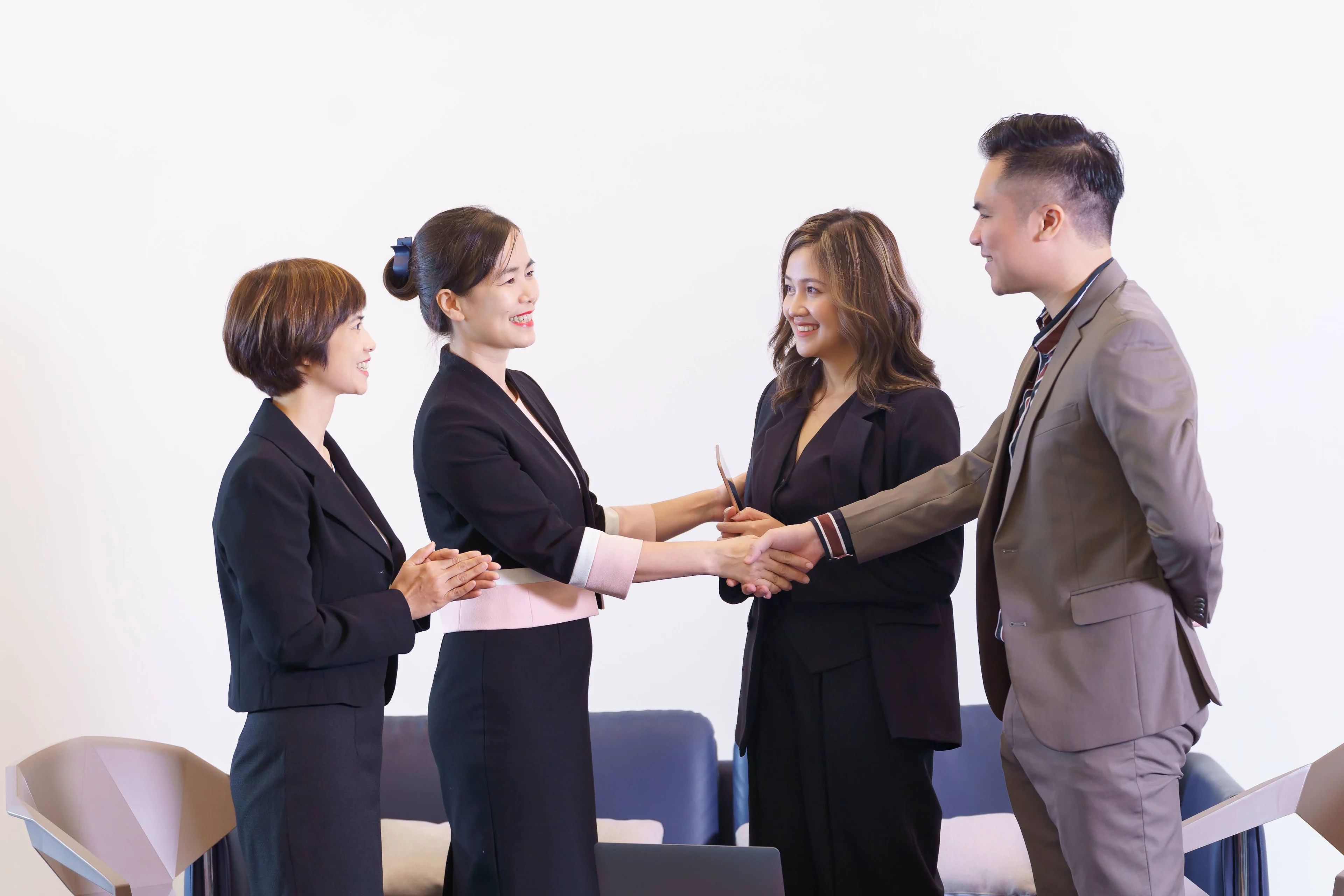 A smiling businesswoman shaking hands with a businessman while colleagues stand by in an office.