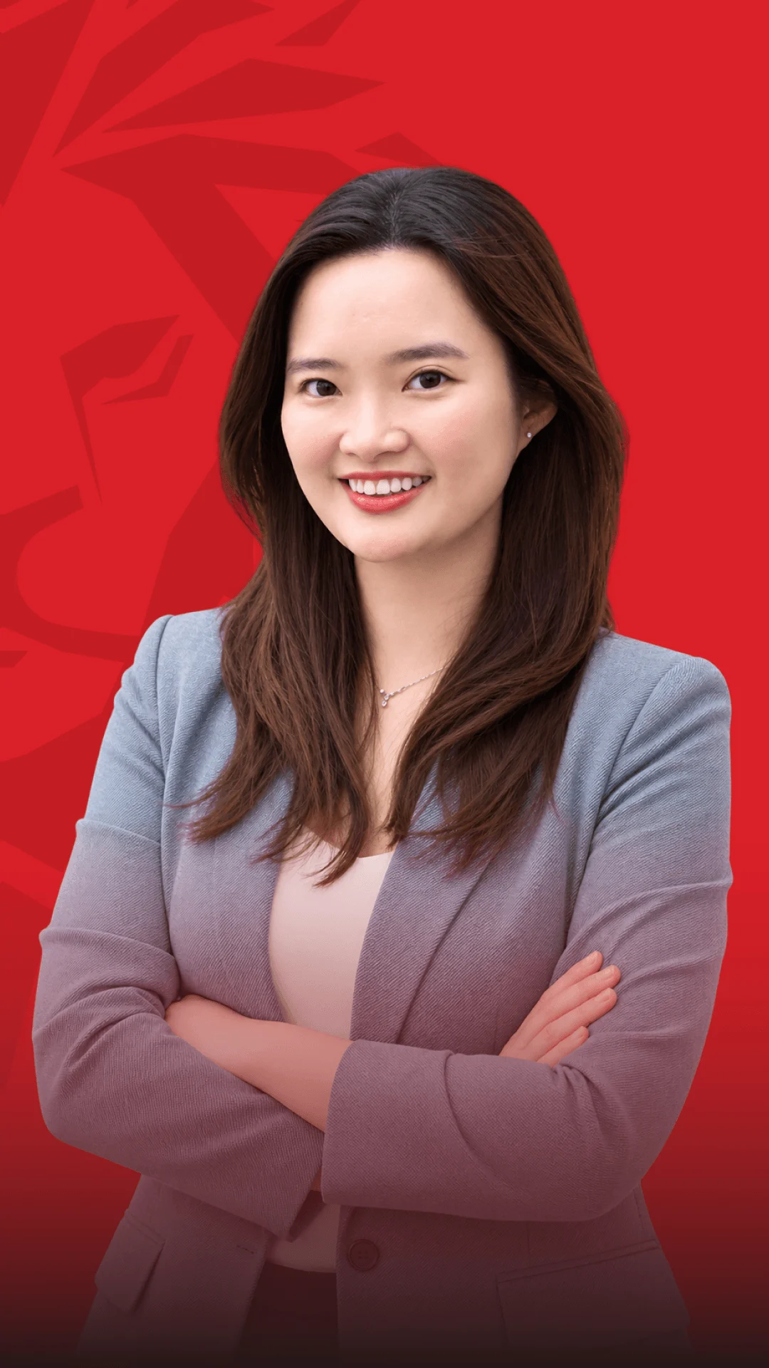 A smiling young woman posing with her arms crossed against a red background, in an alumni portrait.