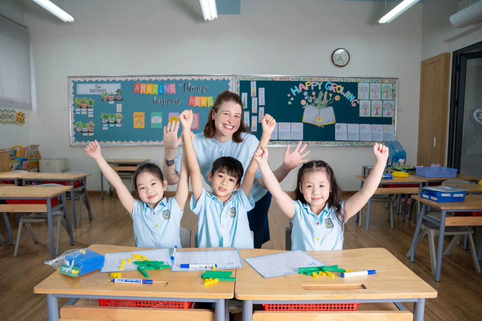 Teacher and three students raising hands during a hands-on maths lesson in a bright classroom.