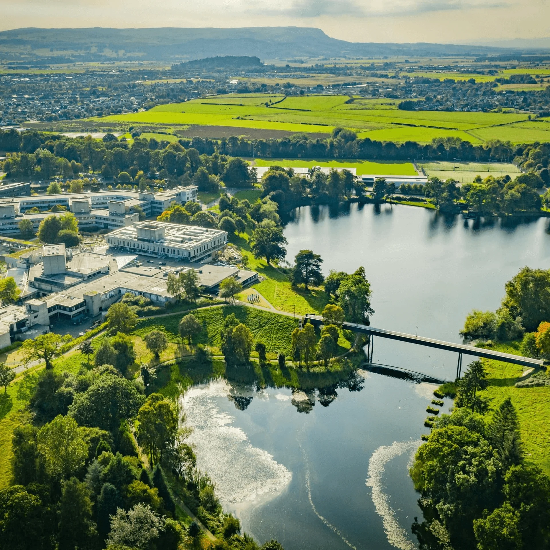 Aerial view of the University of Stirling campus, lake, green fields and surrounding Scottish landscape