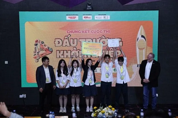 Students and organizers pose onstage at the final round of a Vietnamese competition, with a large colorful “Đấu trường...” event banner and rocket graphic behind them.