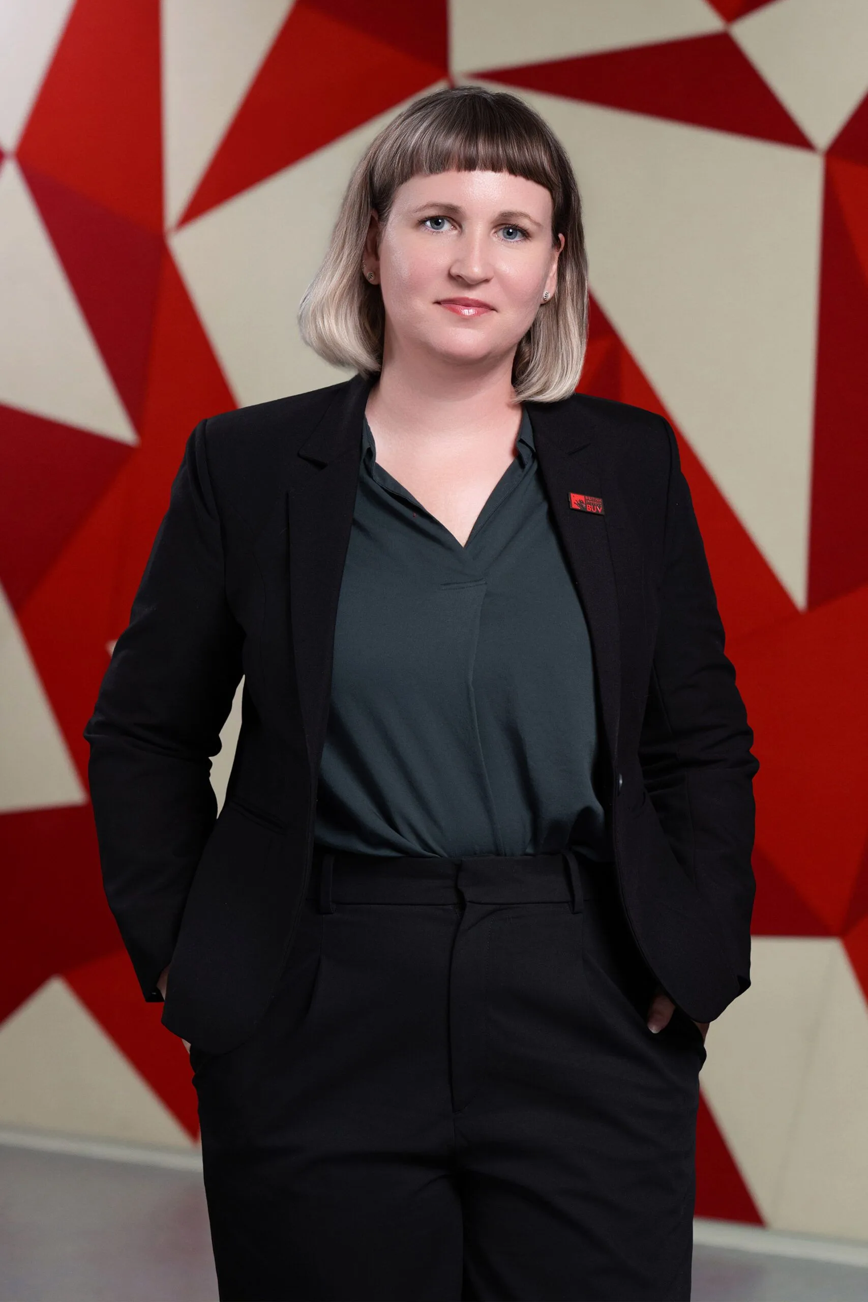 Portrait of a woman in a dark suit standing in front of a red-and-white geometric backdrop.